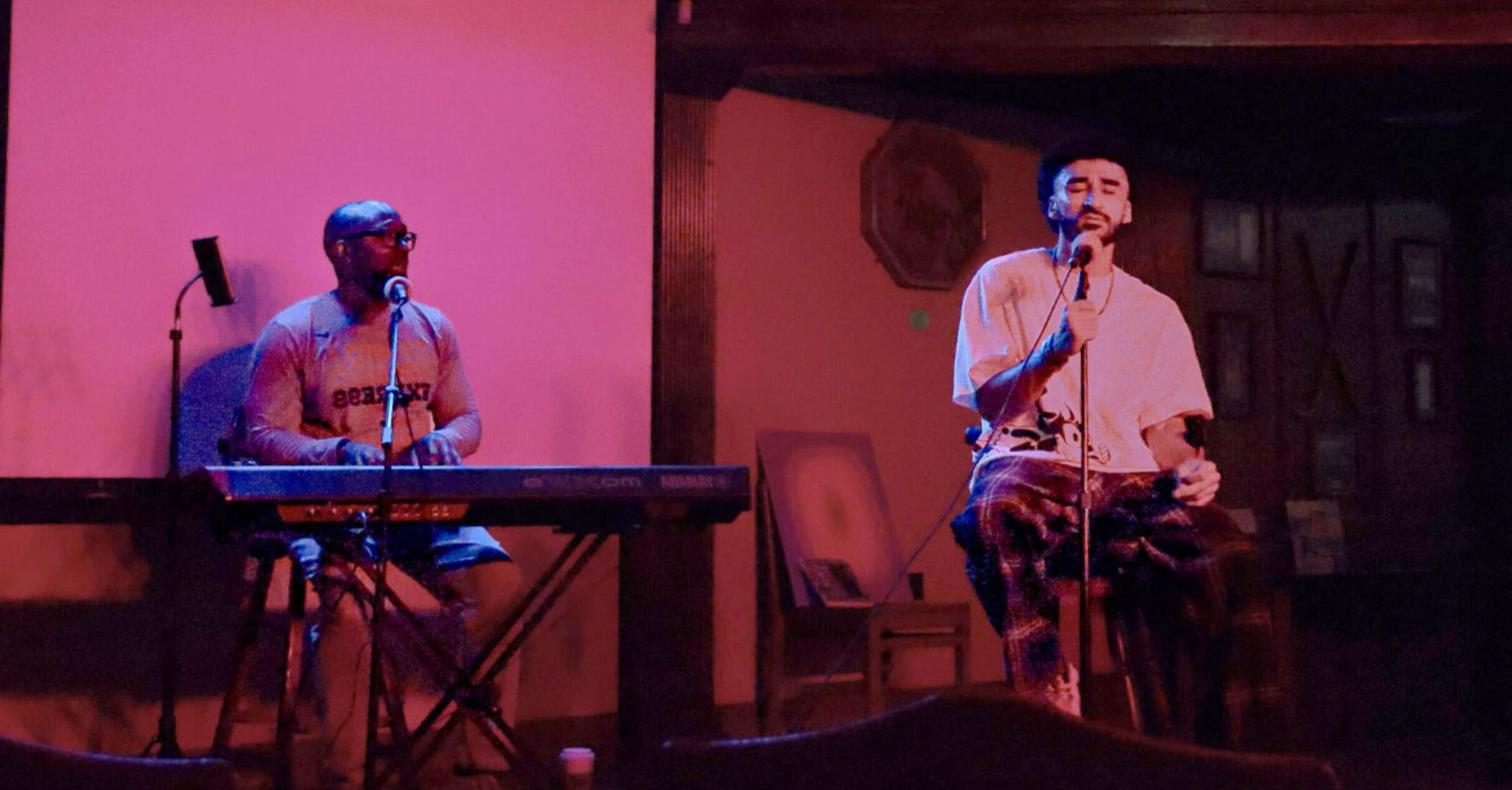 A student performs poetry from the MacKenzie's stage as another student plays a keyboard